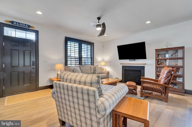 living room with light wood-type flooring, recessed lighting, baseboards, and a glass covered fireplace