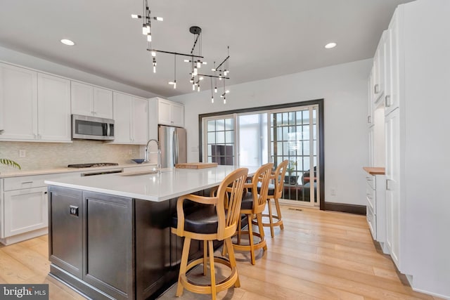 kitchen featuring white cabinets, decorative backsplash, appliances with stainless steel finishes, light countertops, and light wood-style floors