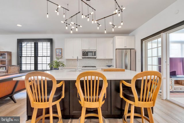 kitchen with a kitchen island with sink, light countertops, appliances with stainless steel finishes, and light wood-style flooring