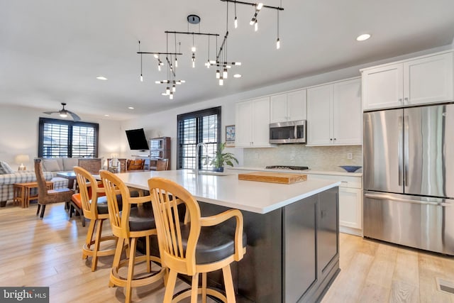 kitchen featuring stainless steel appliances, open floor plan, light wood finished floors, and tasteful backsplash