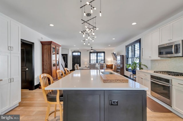 kitchen with stainless steel appliances, backsplash, light wood-style floors, white cabinets, and a sink