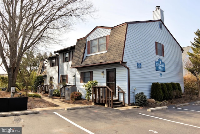 exterior space with a shingled roof, uncovered parking, central AC unit, and a gambrel roof