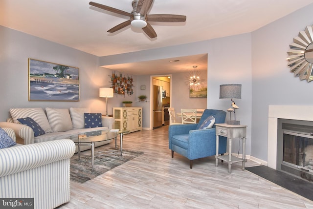 living room with a fireplace with flush hearth, ceiling fan with notable chandelier, wood finished floors, and baseboards