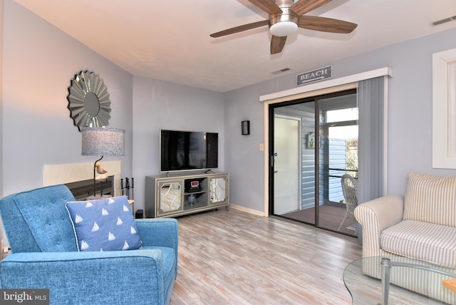 living area featuring a ceiling fan, visible vents, baseboards, and wood finished floors