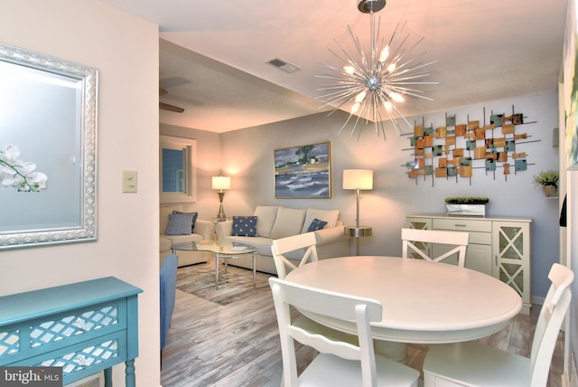 dining space with wood finished floors, visible vents, and an inviting chandelier