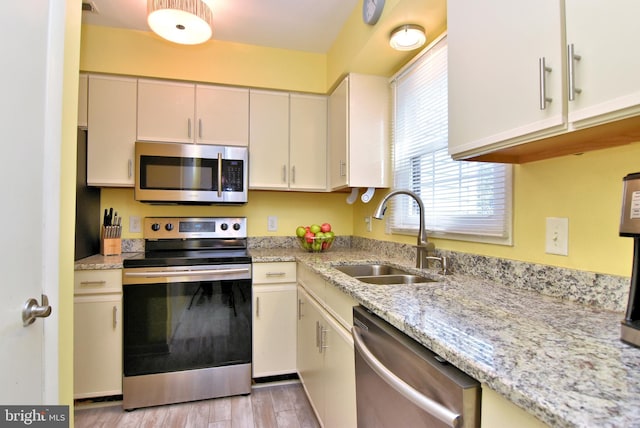 kitchen featuring light wood-type flooring, light stone countertops, stainless steel appliances, and a sink