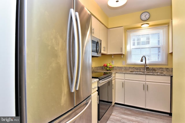 kitchen featuring light wood-type flooring, white cabinets, stainless steel appliances, and a sink