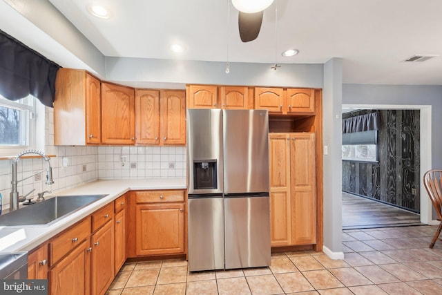 kitchen featuring light tile patterned flooring, a sink, a ceiling fan, stainless steel refrigerator with ice dispenser, and decorative backsplash