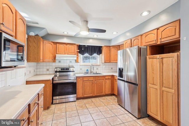 kitchen with under cabinet range hood, a sink, light countertops, appliances with stainless steel finishes, and tasteful backsplash