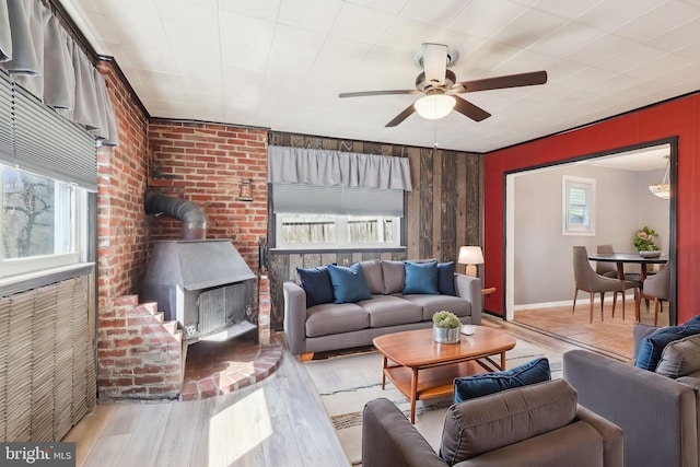 living room featuring wooden walls, baseboards, ceiling fan, wood finished floors, and a wood stove