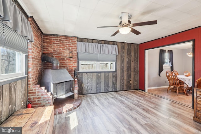 living area with a wood stove, wooden walls, a ceiling fan, and wood finished floors