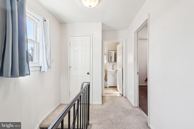 hall with light carpet, a sink, and baseboards