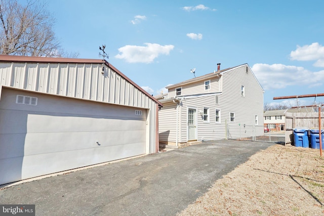 rear view of property with a garage, fence, and an outbuilding