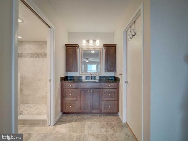 full bathroom featuring a tile shower, vanity, and baseboards