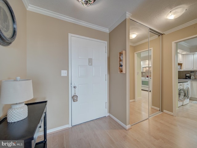 entrance foyer with a textured ceiling, ornamental molding, washer / dryer, and light wood-style flooring