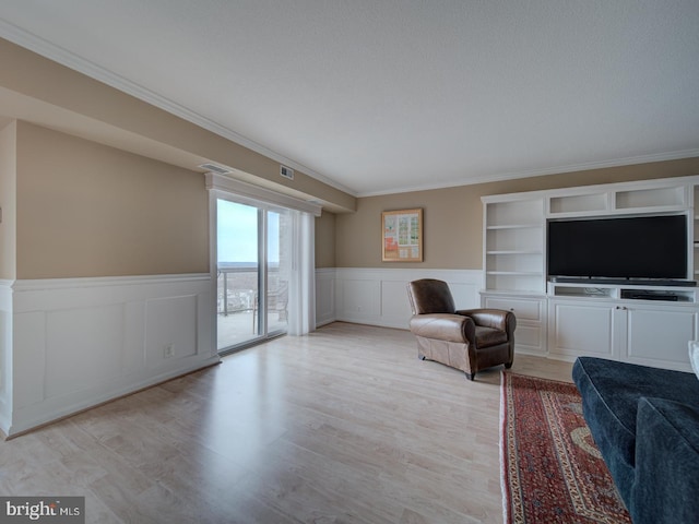 sitting room with wainscoting, visible vents, crown molding, and light wood finished floors