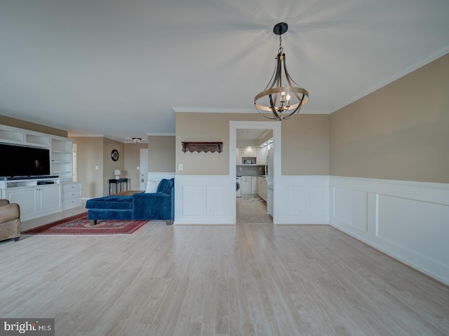 unfurnished living room with a wainscoted wall, independent washer and dryer, an inviting chandelier, crown molding, and light wood-type flooring