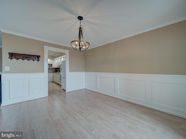 unfurnished dining area featuring a wainscoted wall, light wood-style flooring, crown molding, and a notable chandelier