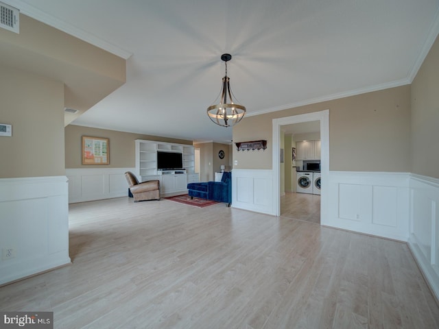 unfurnished room with visible vents, washer and clothes dryer, ornamental molding, light wood-type flooring, and a notable chandelier