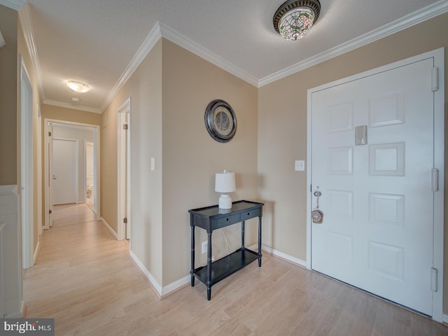 foyer entrance featuring light wood finished floors, baseboards, ornamental molding, and a textured ceiling