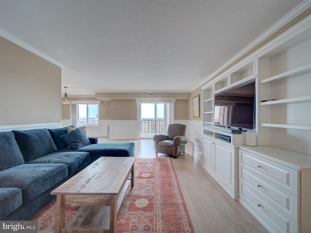 living room with built in features, a wainscoted wall, crown molding, light wood finished floors, and a textured ceiling