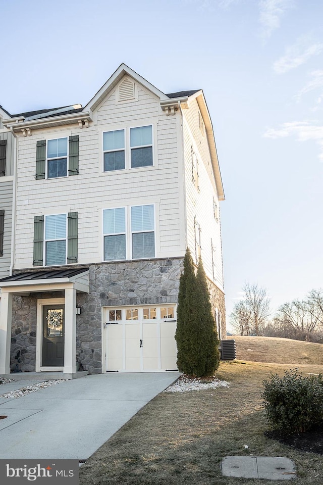 view of front of home featuring driveway, stone siding, an attached garage, and central AC unit