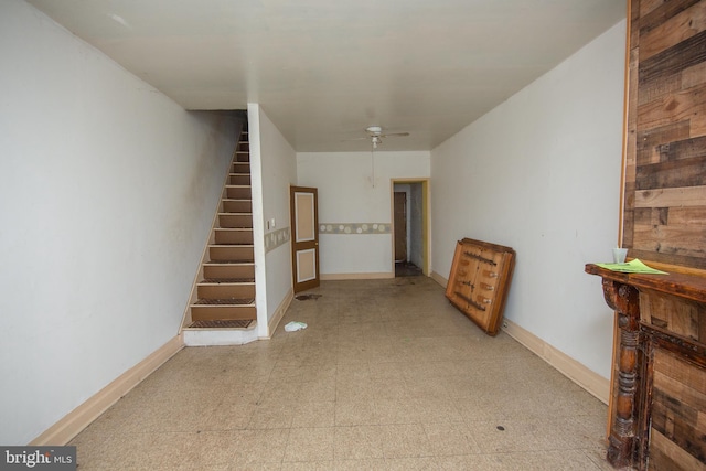 below grade area with stairs, light floors, a ceiling fan, and baseboards