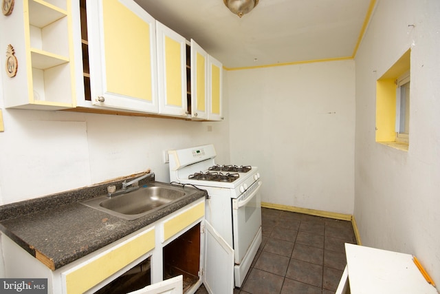 kitchen with white gas stove, dark tile patterned floors, a sink, white cabinets, and dark countertops