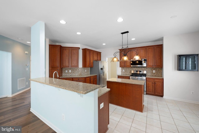 kitchen featuring visible vents, brown cabinetry, a kitchen island, light stone countertops, and stainless steel appliances