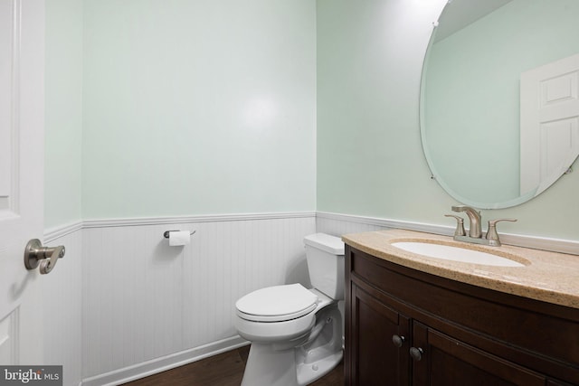 half bath with a wainscoted wall, vanity, toilet, and wood finished floors