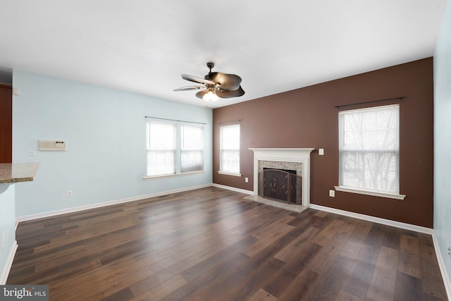 unfurnished living room with a fireplace with raised hearth, ceiling fan, visible vents, baseboards, and dark wood-style floors