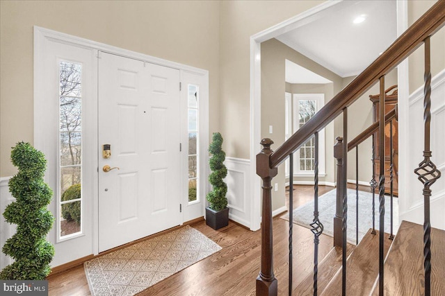 entrance foyer with a decorative wall, wood finished floors, stairs, wainscoting, and crown molding