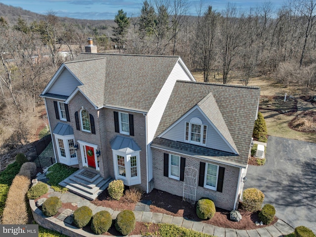 traditional home with roof with shingles, a chimney, a wooded view, and brick siding