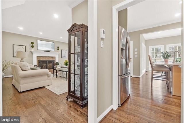 hallway featuring recessed lighting, a sink, wood finished floors, baseboards, and crown molding