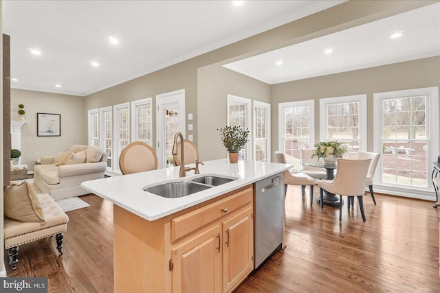 kitchen with wood finished floors, a sink, a kitchen island with sink, light countertops, and stainless steel dishwasher