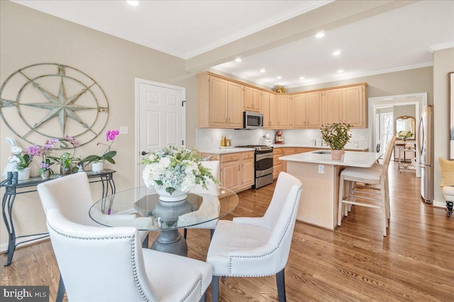 kitchen with a breakfast bar area, light countertops, light wood-style flooring, light brown cabinetry, and appliances with stainless steel finishes