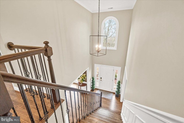 staircase featuring a notable chandelier, a high ceiling, ornamental molding, wainscoting, and wood finished floors