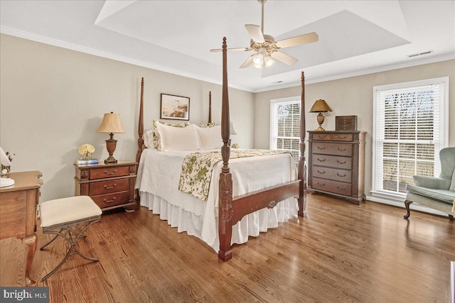 bedroom with ceiling fan, wood finished floors, visible vents, ornamental molding, and a raised ceiling