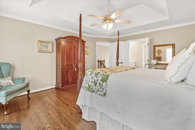 bedroom featuring a raised ceiling, ornamental molding, ceiling fan, wood finished floors, and baseboards