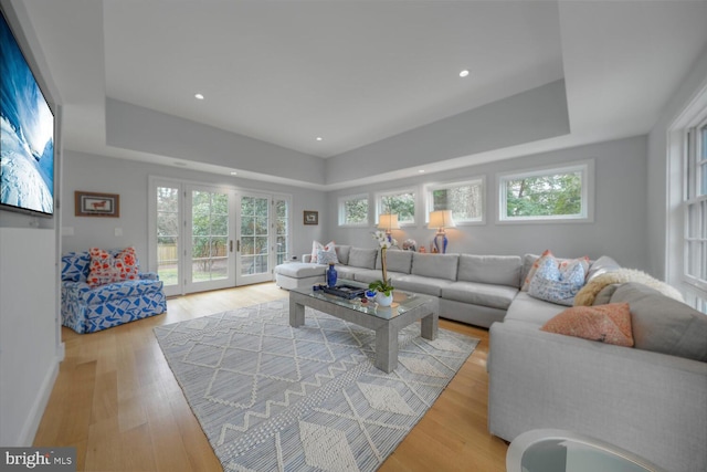 living room featuring recessed lighting, french doors, light wood-type flooring, and a tray ceiling