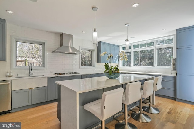 kitchen featuring wall chimney range hood, light wood-style flooring, appliances with stainless steel finishes, and a sink