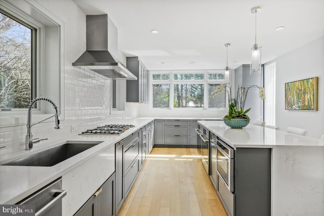 kitchen with gray cabinets, a sink, tasteful backsplash, appliances with stainless steel finishes, and wall chimney range hood