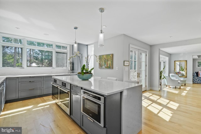 kitchen featuring gray cabinetry, a center island, decorative light fixtures, stainless steel oven, and light wood-style flooring
