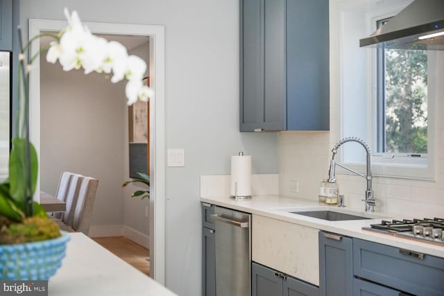 kitchen with a sink, light countertops, dishwasher, wall chimney range hood, and backsplash