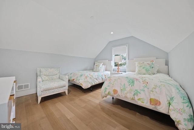 bedroom featuring light wood finished floors, visible vents, and vaulted ceiling