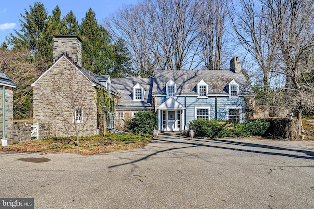 view of front facade featuring stone siding, a high end roof, and a chimney