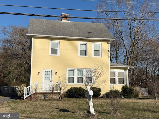 colonial inspired home with a chimney, fence, a front lawn, and roof with shingles