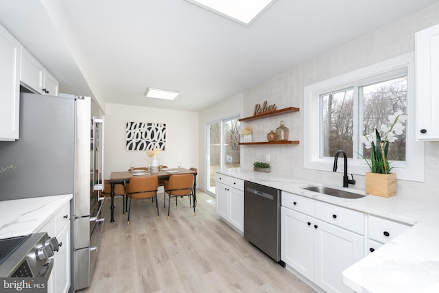 kitchen with light stone countertops, a sink, stainless steel appliances, white cabinetry, and light wood-type flooring