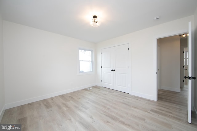 unfurnished bedroom featuring a closet, light wood-style flooring, and baseboards