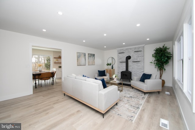 living area with light wood finished floors, visible vents, baseboards, a wood stove, and recessed lighting